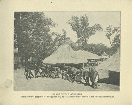 A black and white photograph of some members of the Bontoc Igorrote tribe dancing. Huts constructed out of straw can be seen in the background. 