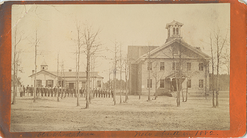 A photograph of the Schofield School houses. Two houses can be seen, one in the foreground and one in the background. Students (and teachers?) are in a line. 