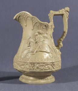 A cream colored ceramic Jug with a carved figure of a knight riding a horse. Detailing is carved onto the rim, base, and handle.